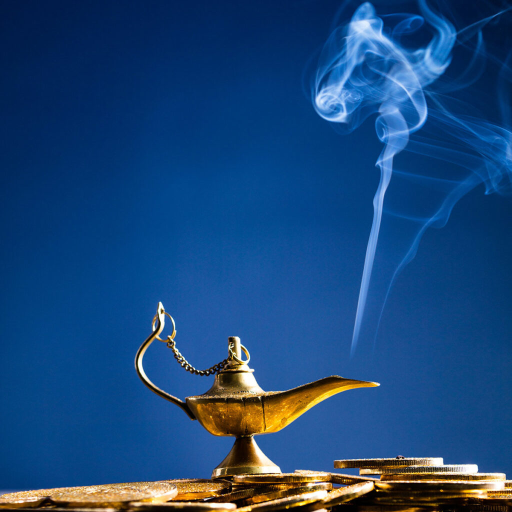 Ilustracja przedstawia Lampę Alladyna, z której wydobywa się dymek. Lampa stoi na monetach.