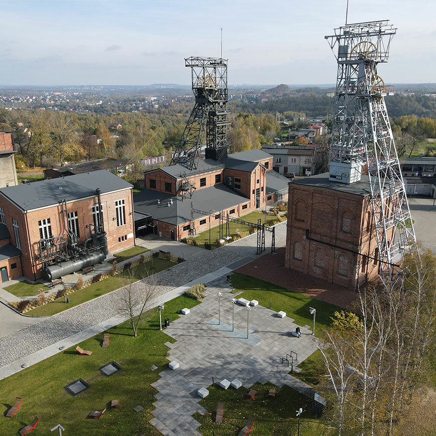 Zdjęcie zostało wykonane z lotu ptaka. Przedstawia dwie stalowe wieże szybowe kopalni, budynki nadszybia oraz inne obiekty zabudowy, a także tereny zielone.