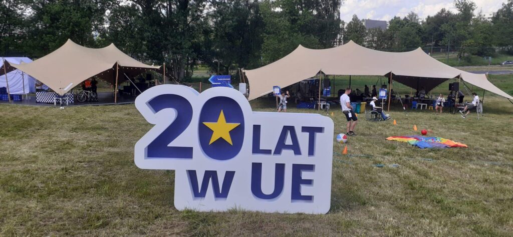 Zdjęcie przedstawia szyld 20 lat w UE, który został ustawiony w Parku Środulskim podczas pikniku. 