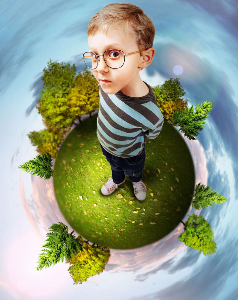Ilustracja przedstawia małego chłopca w okrągłych okularach, z zaciekawioną miną, stojącego na pomniejszonej kuli ziemskiej porośniętej drzewami.