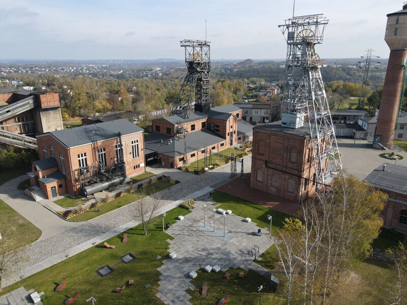 Zdjęcie zostało wykonane z lotu ptaka. Przedstawia dwie stalowe wieże szybowe kopalni, budynki nadszybia oraz inne obiekty zabudowy, a także tereny zielone.