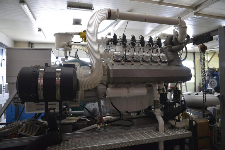 Zdjęcie wielkiego silnika. Widoczna jest komora, z której wychodzi duża rura biegnąca do innego elementu. U dołu strony znajduje się jeszcze jedna fotografia, na której widzimy mężczyznę w ochronnej masce, spawającego rurę.