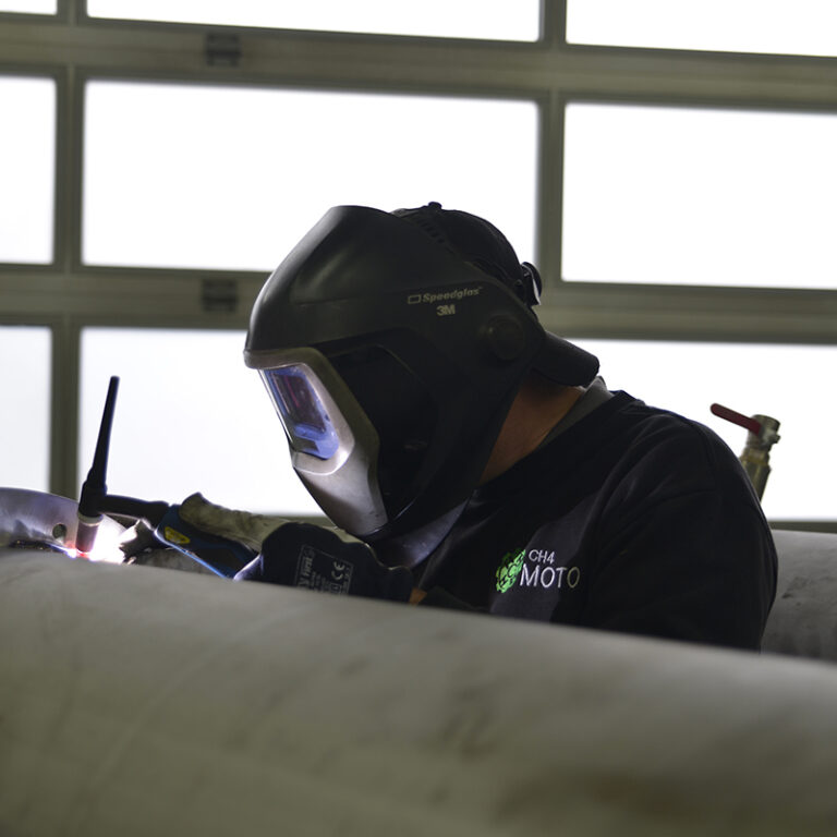 Zdjęcie przedstawia pracownika w stroju roboczym z napisem CH4 Moto i ochronnej masce.