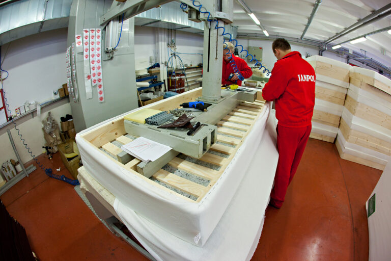 Na ilustracji widać dwóch mężczyzn w czerwonych uniformach, którzy obsługują maszynę.