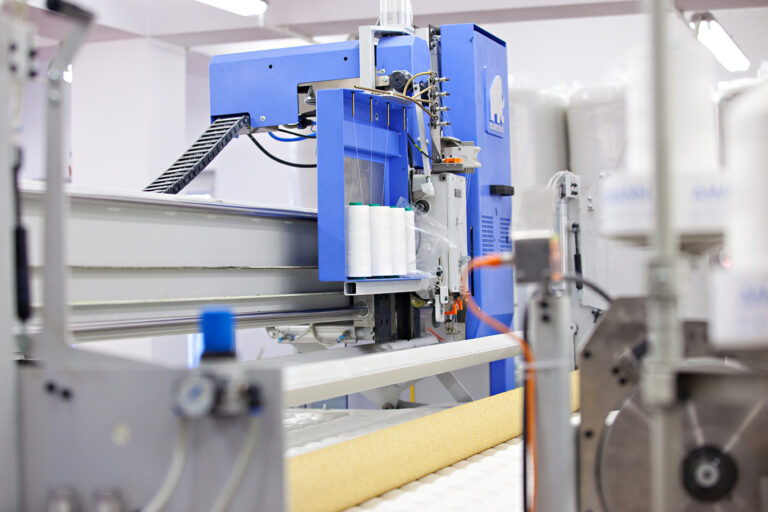 Zdjęcie to zbliżenie na maszynę szwalniczą. Widoczne są między innymi założone rolki nici.