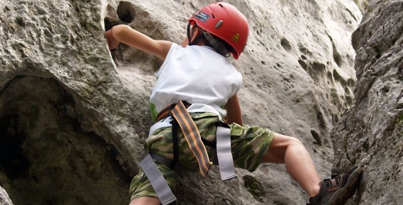 Ilustracja przedstawia chłopca w czerwonym kasku, który wspina się na skały.