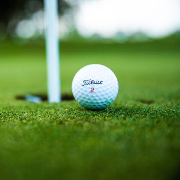 Zdjęcie przedstawia piłeczkę golfową blisko dołka golfowego. Murawa wokół ma kolor zielony.