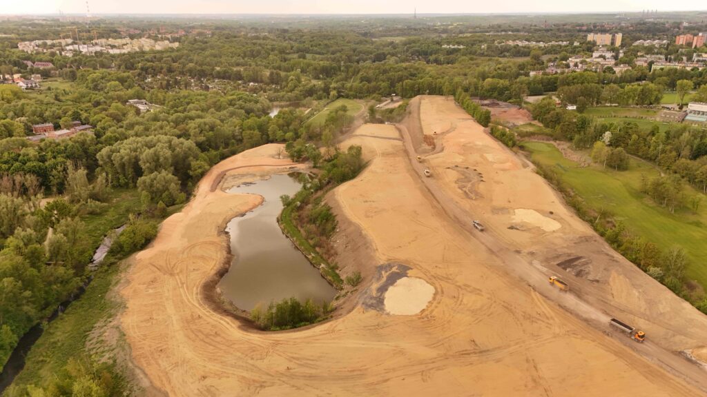 Ujęcie z drona na inwestycję Armada Bytom. Fotografia przedstawia trwające pracę nad polem golfowym. Na środku dostrzegalny jest zbiornik wodny.