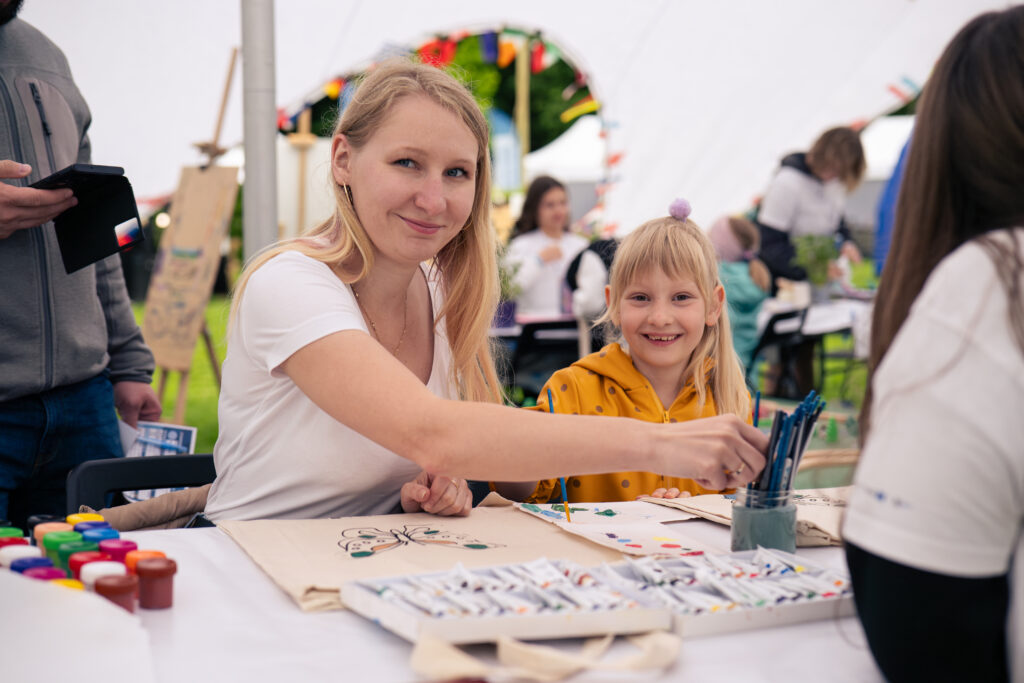 Uśmiechnięte kobieta oraz dziewczynka malują wzór motyla na ekologicznej torbie.