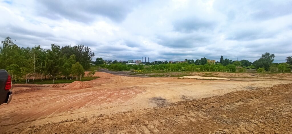 Zdjęcie przedstawia początkową fazę inwestycji Armada Bytom. Na fotografii widoczny jest rozkopany piach a w oddali widać tereny zielone.