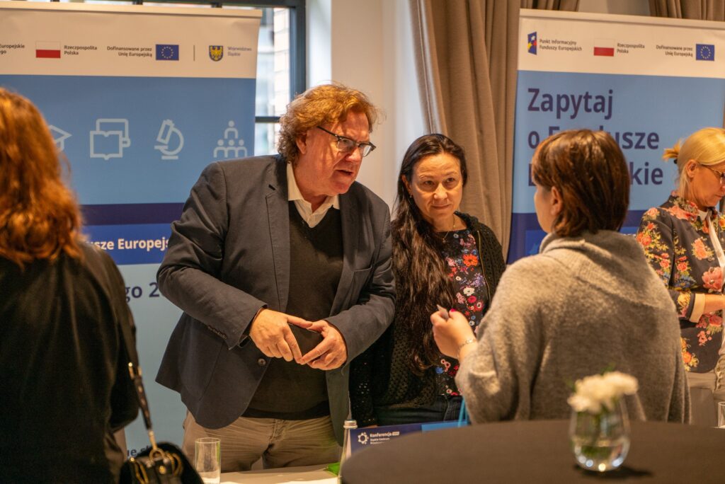 Zdjęcie ukazuje grupę ludzi rozmawiających przy stoisku informacyjnym.