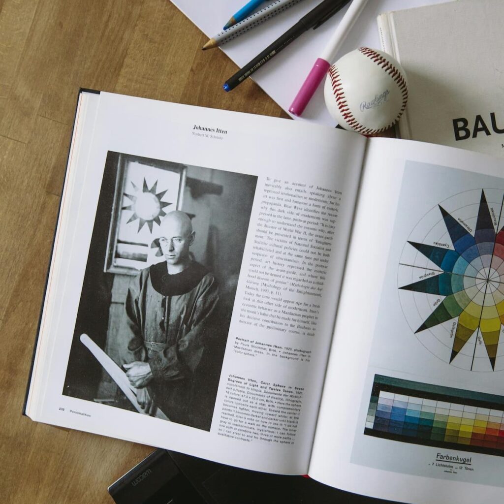 Otwarta książka o teorii koloru, leżąca na biurku obok tabletu graficznego, przedstawiająca portret Johannesa Ittena. Obraz nawiązuje do kryterium realizacji zasad Nowego Europejskiego Bauhausu, łączącego estetykę, zrównoważenie i brak barier w nowych inwestycjach.